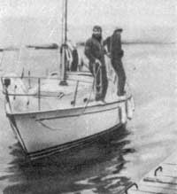 Два члена команды стоят около вант, готовясь ступить на берег с носовым и кормовым продольными концами.